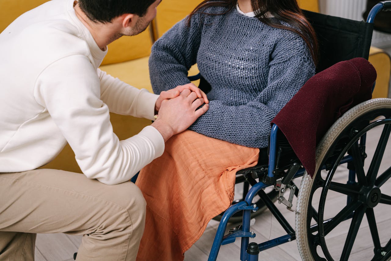 who-we-are Man providing care and support to woman in a wheelchair indoors.