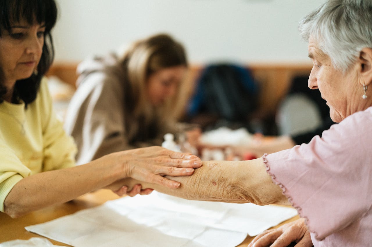 A caregiver gently supports an elderly woman's arm during a community activity.
